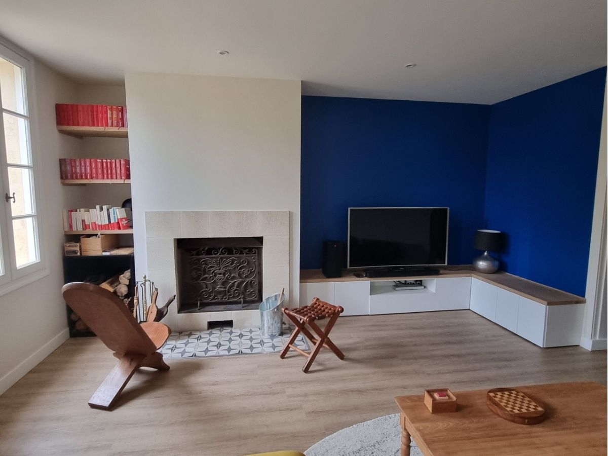 Salon avec cheminée modernisée et meubles sur-mesure cheminée modernisée avec pierre naturel, étagères en bois massif, banc TV sur-mesure et mur bleu - Consultante en aménagement intérieur en Gironde